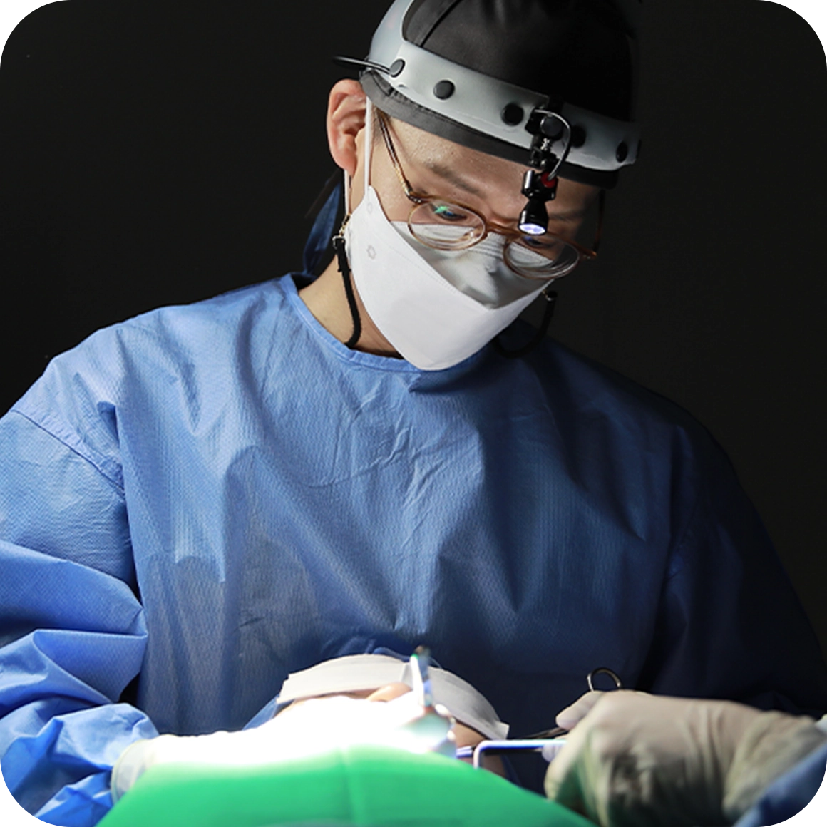 手術用マスクとヘッドライトを装着した医師。345 Plastic Surgeryの美容整形手術の様子。メスを持つ手元。医療、美容関連のイメージ。